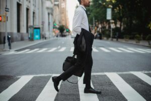 A businessman crosses a city street with jacket in hand, portraying urban elegance.